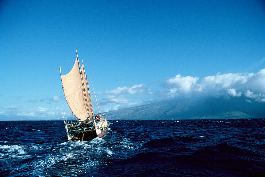 A sailing canoe heads toward an island in the distance at full sail.