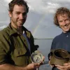 Two men each hold a ceramic vessel at the archaeological excavation