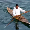 a man in a white hooded sweatshirt paddles in a skin boat kayak