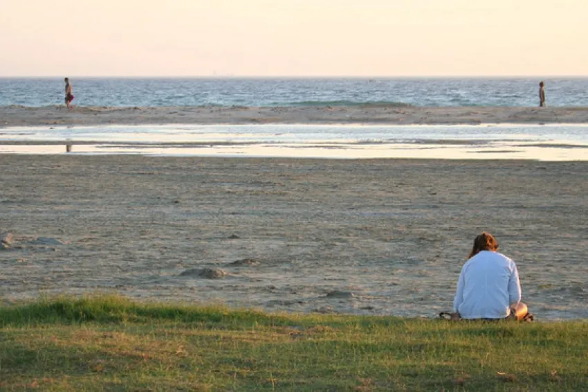 A woman sits on the beach reading a book.