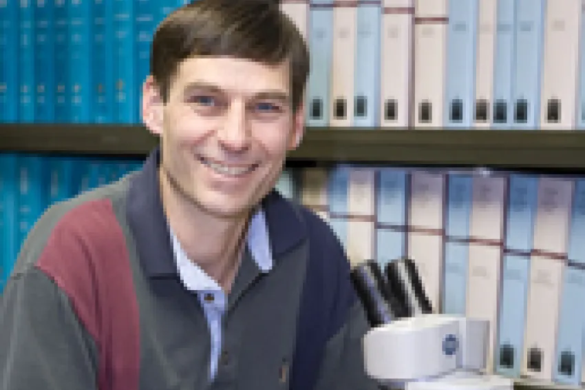Image of Brian Huber looking at camera next to microscope.