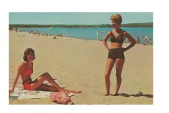 a woman sunbathes on a beach and another stands to her side in a bikini