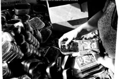 a woman's hands close a tin of sardines near a pile of empty cans
