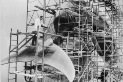 a sculptor works on a huge blue whale model in scaffolding