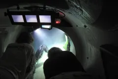 Two scientists peer out into the ocean from inside the Curasub, a 5-person submersible 