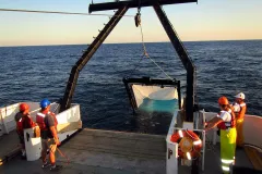 scientists in life jackets await the retrieval of a big net off the back of ship