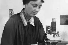 scientist Drew-Baker reads a book by her microscope