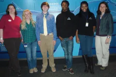 Students studying climate change pose for a photo against a wall.
