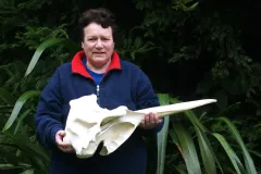 a Māori woman in a navy blue fleece holds the skull of a beaked whale