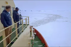 two men on the deck of a ship assessing the ice in the ocean