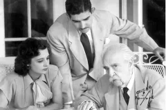 a young woman, young man, and elderly man discuss around a wire frame table outside
