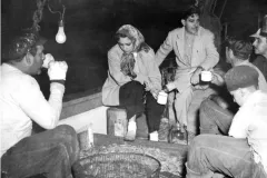 a woman in a shawl with men drinking on a boat with a huge crate of shrimp
