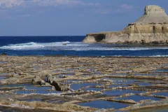 shallow pans carved out of the sea coast create many pools with a seascape in the background