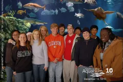 Students pose in front of an aquarium tank with fish.