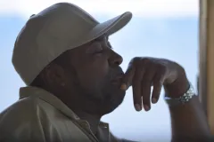 a man sits pondering with a tan ball cap on