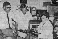 a woman with clipboard and two male assistants