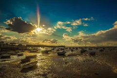 boats sit in the mud at low tide underneath a sunset
