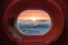an ocean sunrise through a red metal hole