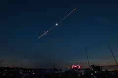 A dark sky with each stage of the solar eclipse above neon signs. 