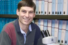 Image of Brian Huber looking at camera next to microscope. 