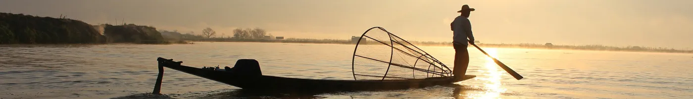 A man looks out at sea while standing on a low, artisanal fishing boat. 