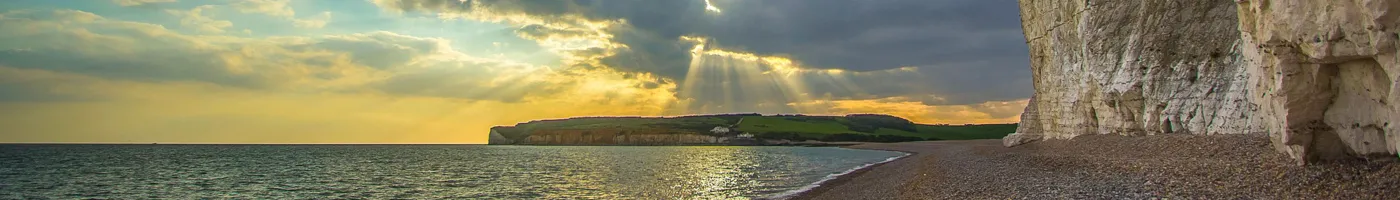 Sun rays shine on an ocean coast with a steep rocky coast. 