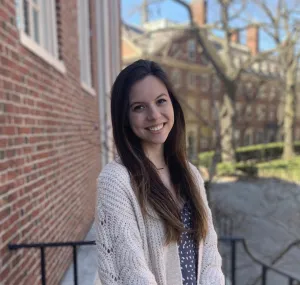 A headshot of Madison Golberg wearing a white sweater with long brown hair.