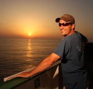 Brandon Southall leaning on a boat railing with a sunset in the background.