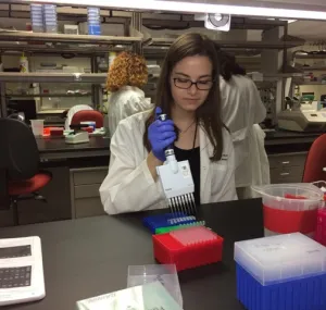 Sarah Leinbach wearing a white lab coat as she does work in a lab.
