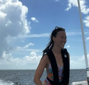 a person in a white bathing suit smiles by the ocean