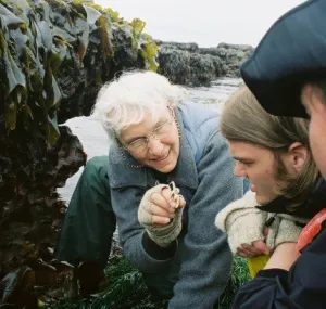 Megan N. Dethier kneeling on a rocky shoreline with two other people. 