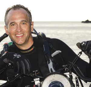 Brian Skerry wears scuba gear standing in the ocean. 