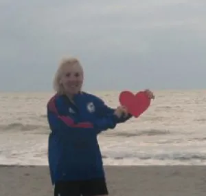 Colleen Marzec standing on the beach holding a cut out red heart.