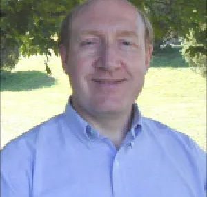 Isaac Ginis smiling at camera with grass and trees in background.