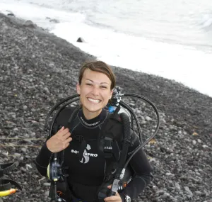 Maggy Hunter Benson in SCUBA gear on the shore of the ocean.