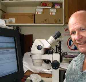 Douglas Fenner sitting at a desk with a computer and a microscope.