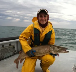 Ellen Spooner on a boat in full yellow rain gear holding a large fish.