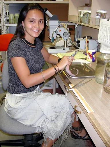 a young scientist with long black hair sits at her desk