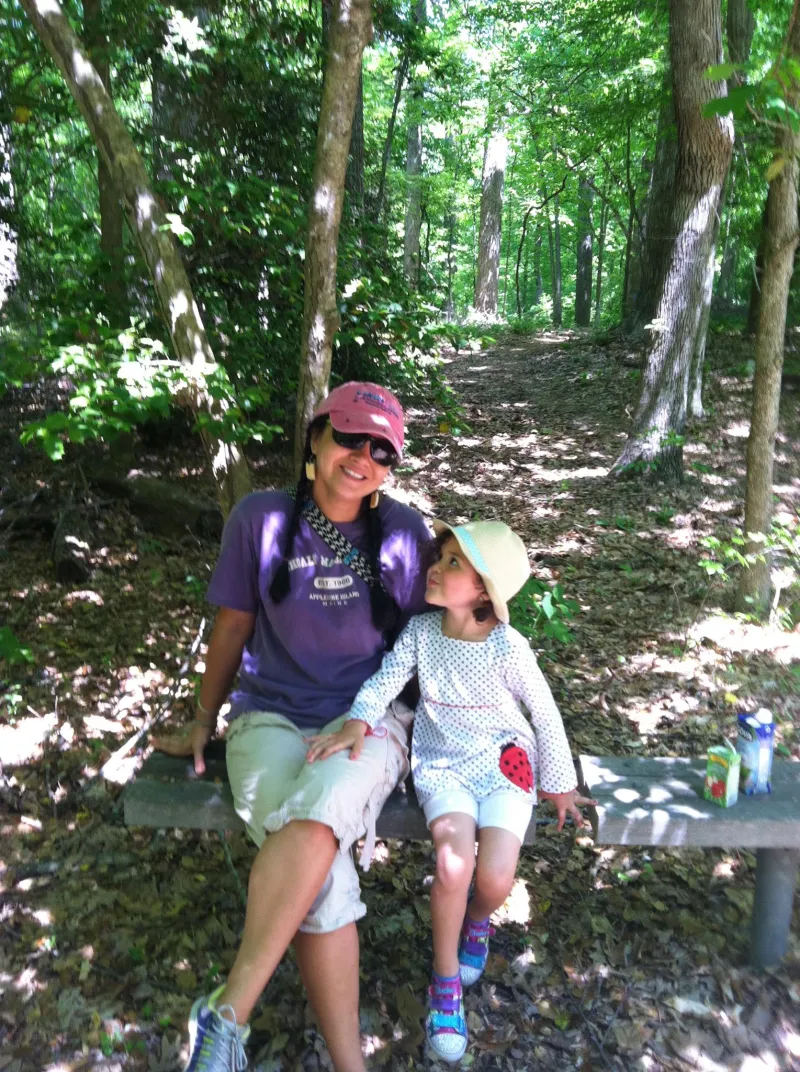 a young mother in colorful hiking attire sits on a bench with her young daughter
