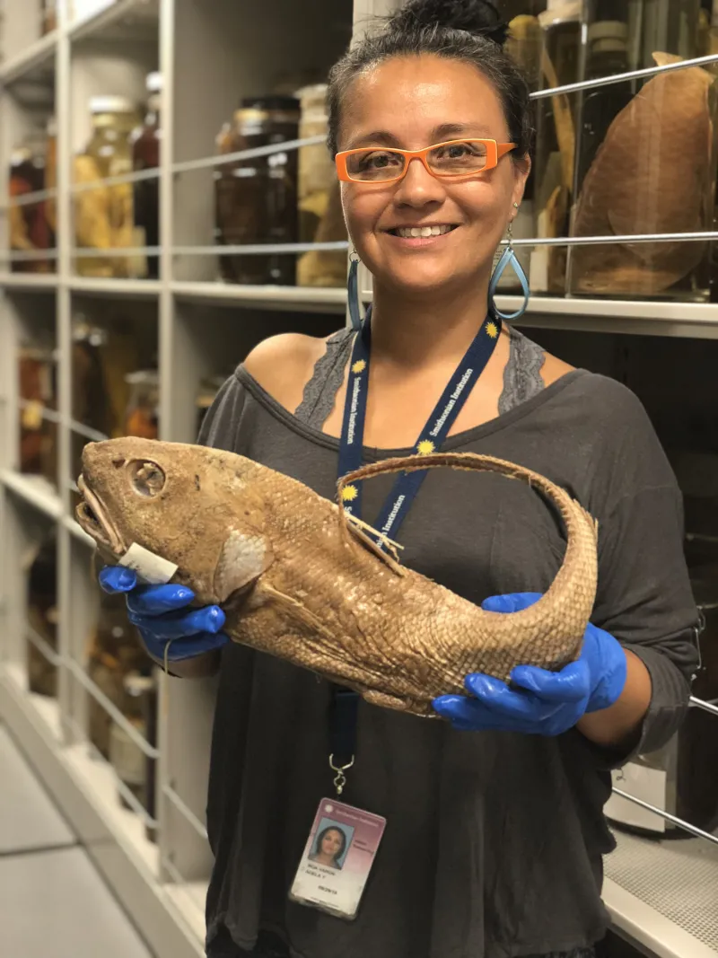 a female scientist with orange glasses holds a preserved fish