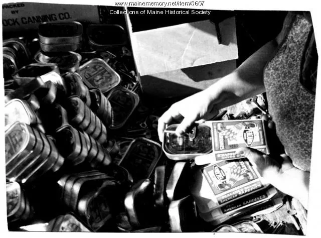 a woman's hands close a tin of sardines near a pile of empty cans