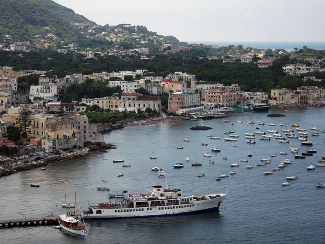 A photo of a seaside town with boats docked in the harbor and buildings along the shore. 