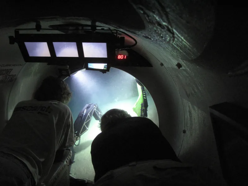 Two scientists peer out into the ocean from inside the Curasub, a 5-person submersible