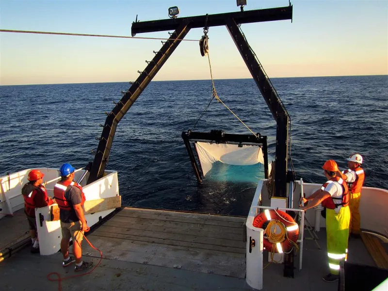 scientists in life jackets await the retrieval of a big net off the back of ship