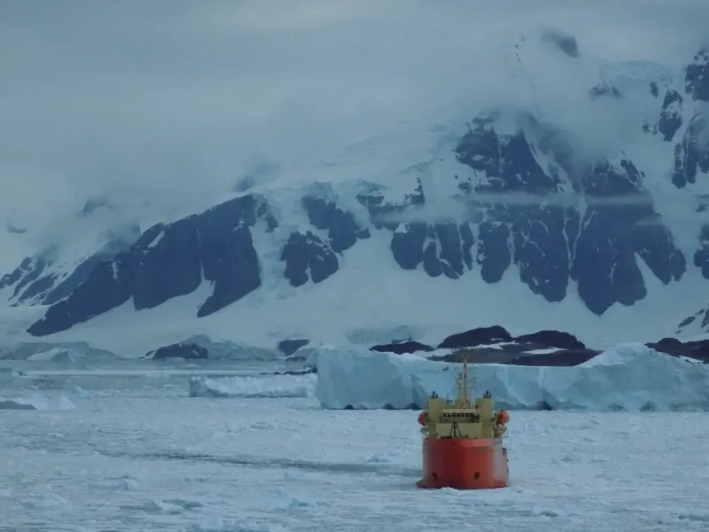 A large red research vessel among icy waters and snowy mountains