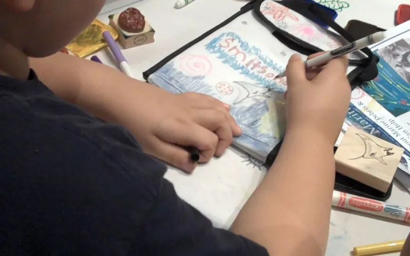 A student uses a marker to decorate a reusable lunch bag with ocean creatures