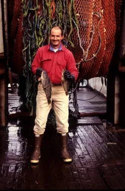 George Watters on the deck of a boat holding two fish. 