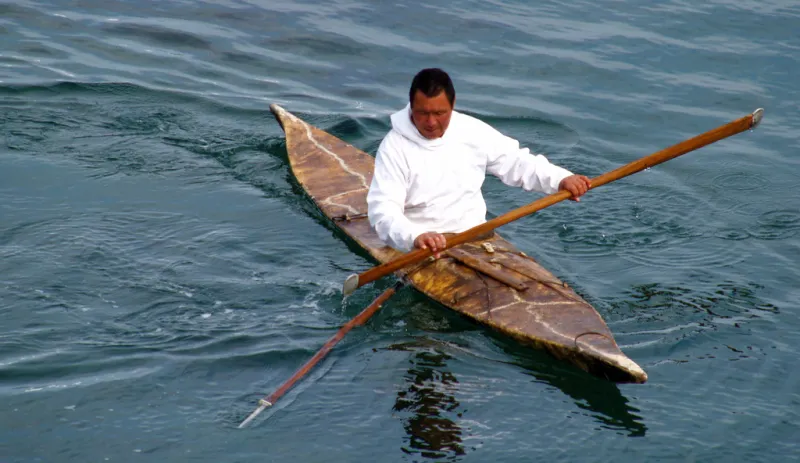 a man in a white hooded sweatshirt paddles in a skin boat kayak