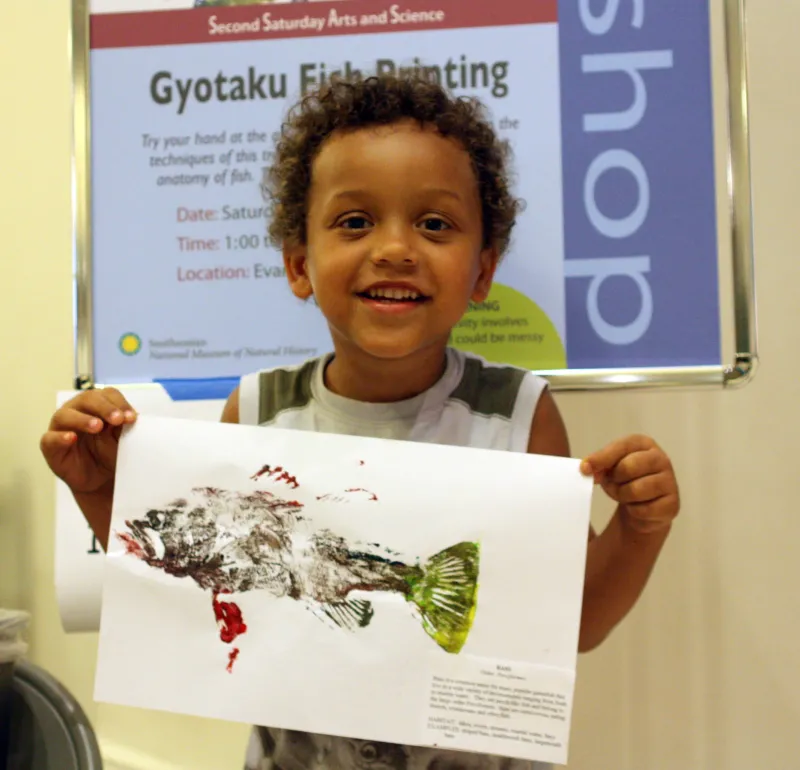 A young visitor holds up his painted fish Gyotaku fish print at the Smithsonian's National Museum of Natural History