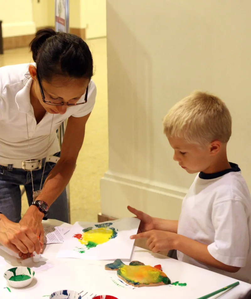 A teacher and a young boy paint a fish mold to create a Gyotaku style print